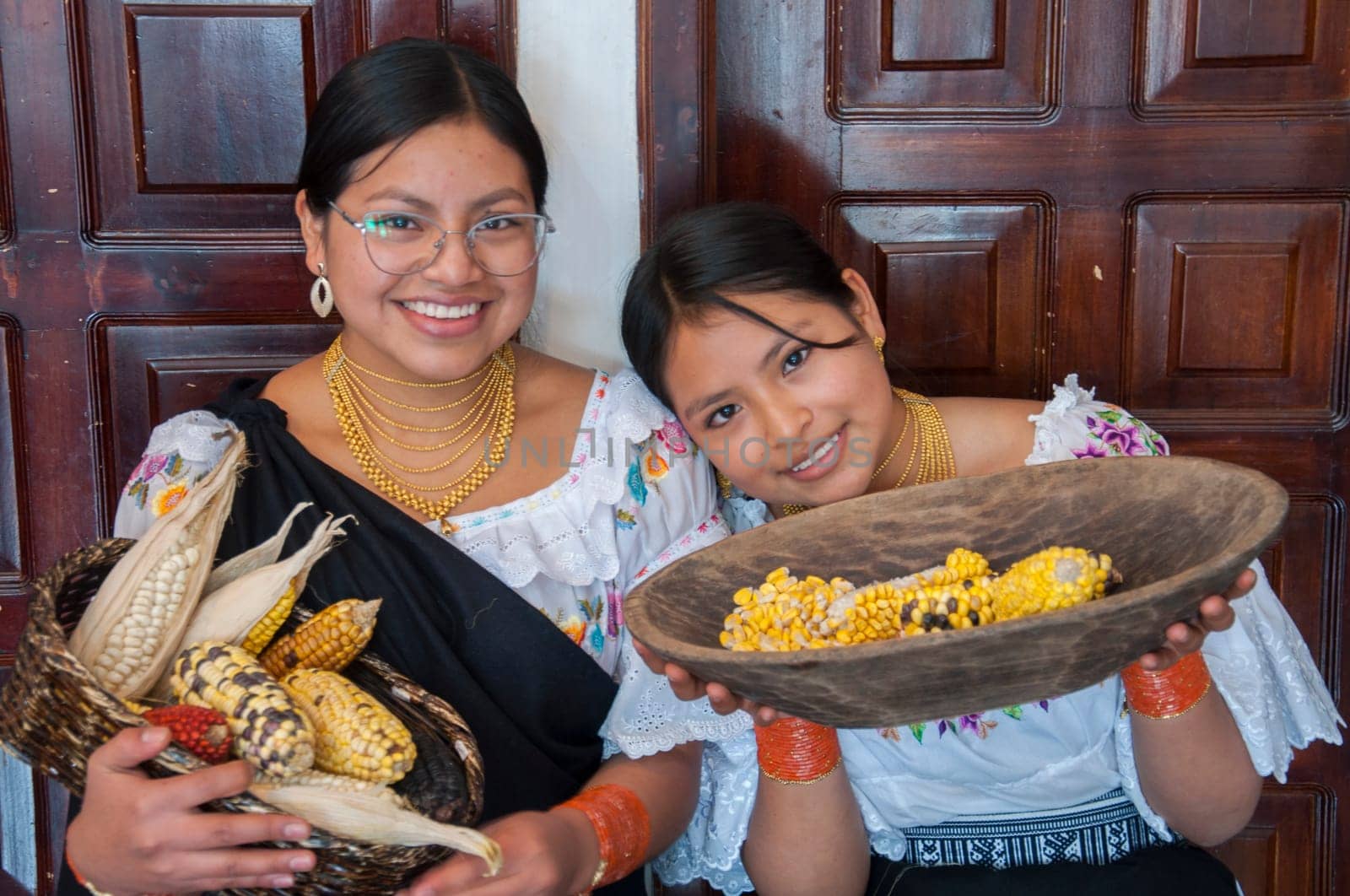 two smiling indigenous people from otavalo in traditional dress showing a basket with the harvest of ears of corn. High quality photo