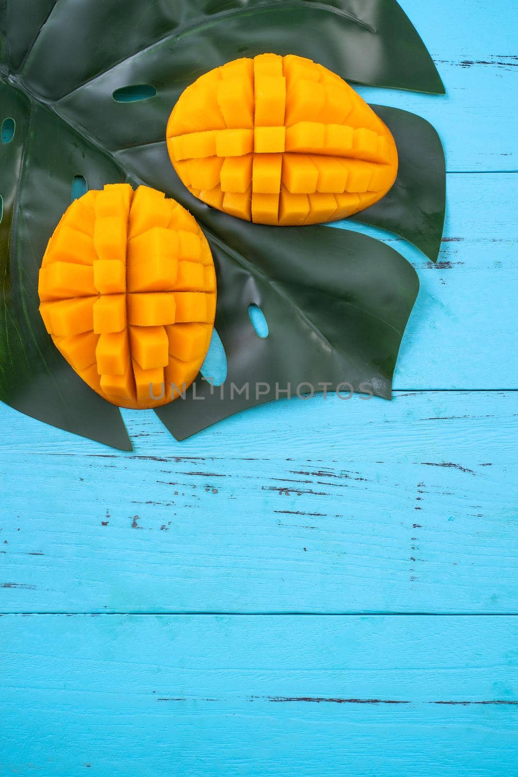 Mango - Fresh chopped tropical mango fruit isolated on bright vibrant light blue wooden table background, top view, flat lay layout, overhead shot. by ROMIXIMAGE