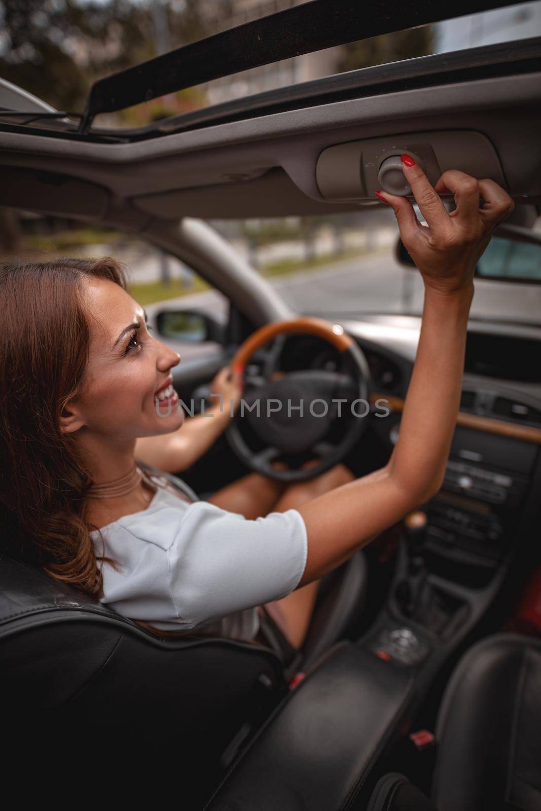 Beautiful young lady is opening the roof window while driving a car.