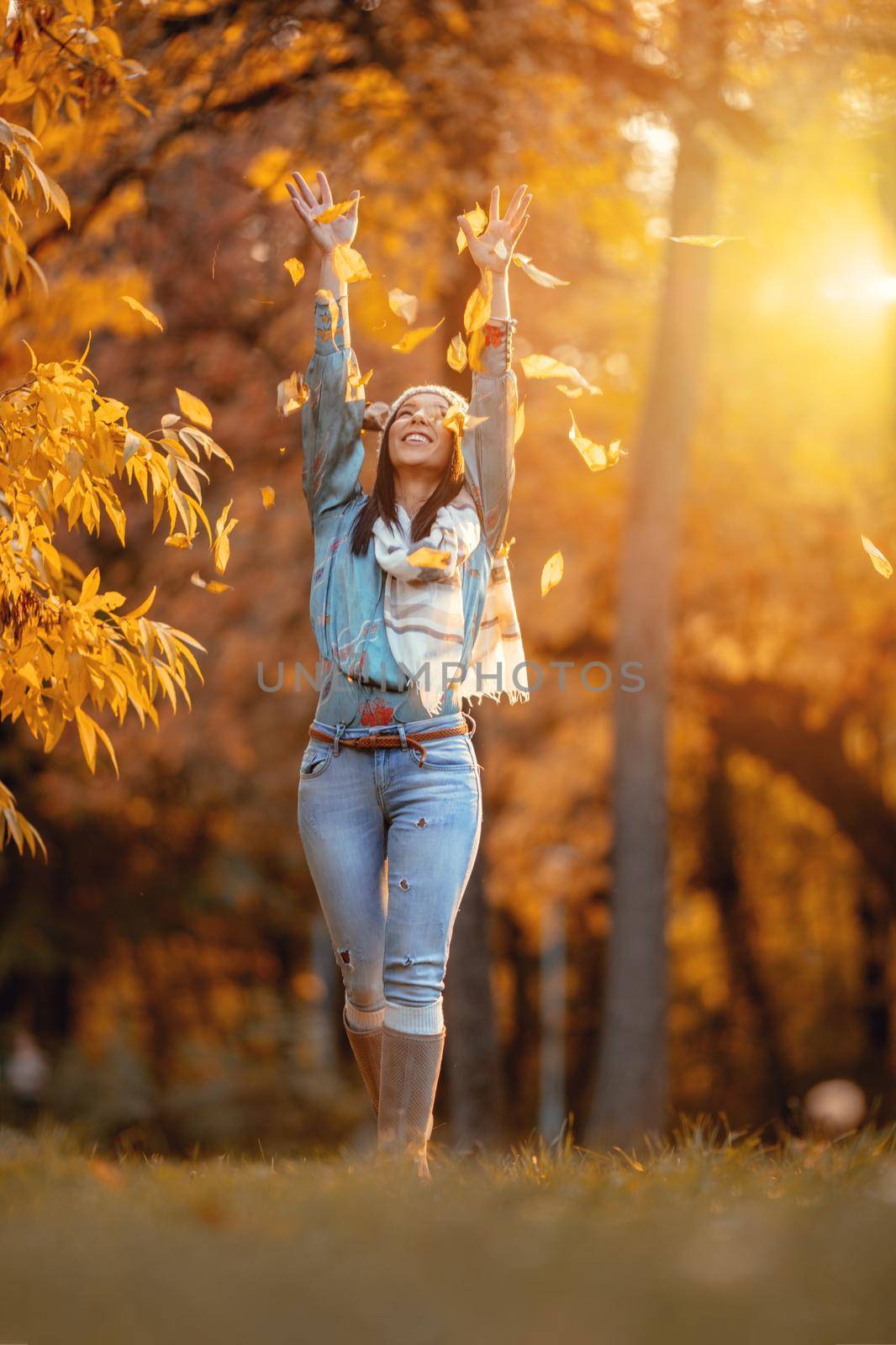 Cheerful young beautiful woman going alone in the park and throws leaves up in golden sunny autumn.