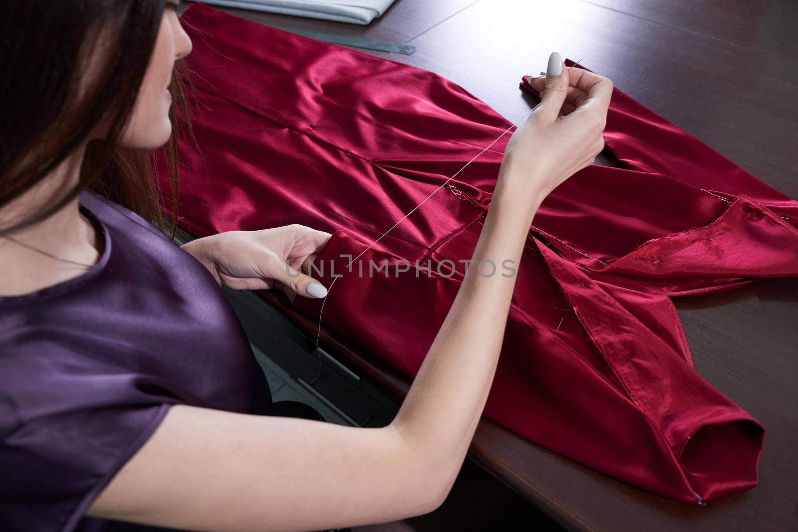 Beautiful young dressmaker in workroom sewing red dress
