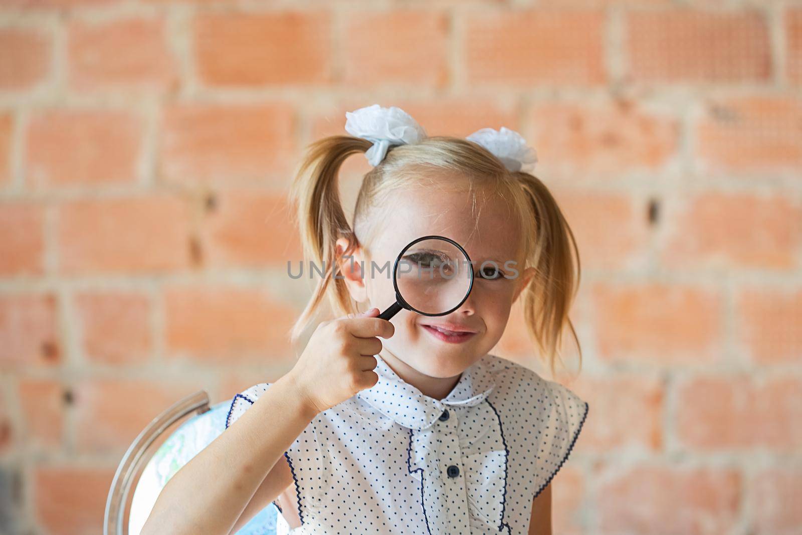 Cute little girl in school uniform with magnifier if front of her eye, back to school concept