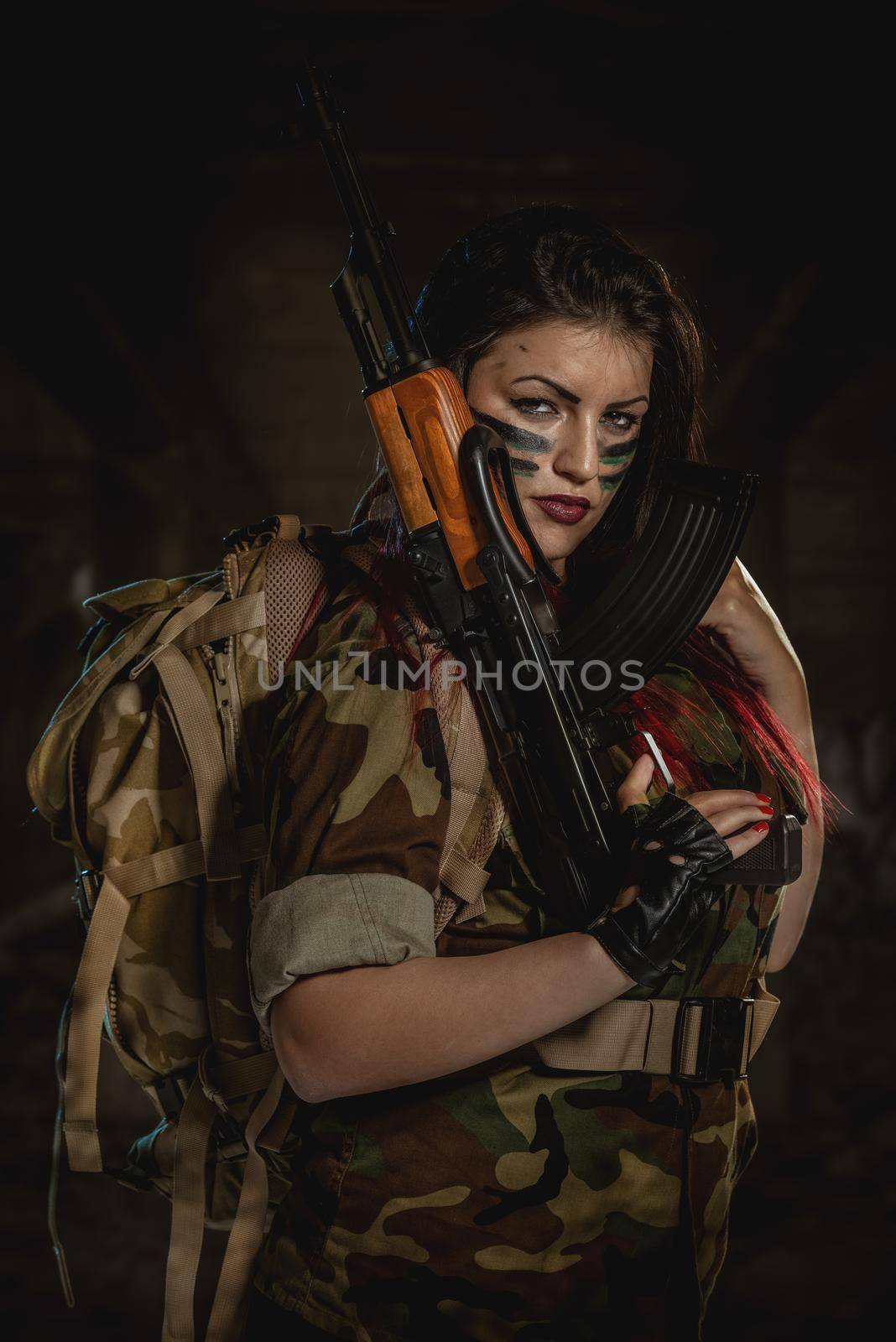 Attractive dark-haired girl in camouflage shirt hold machine gun leaning on the shoulder and with a dangerous expression on her face looking at the camera.