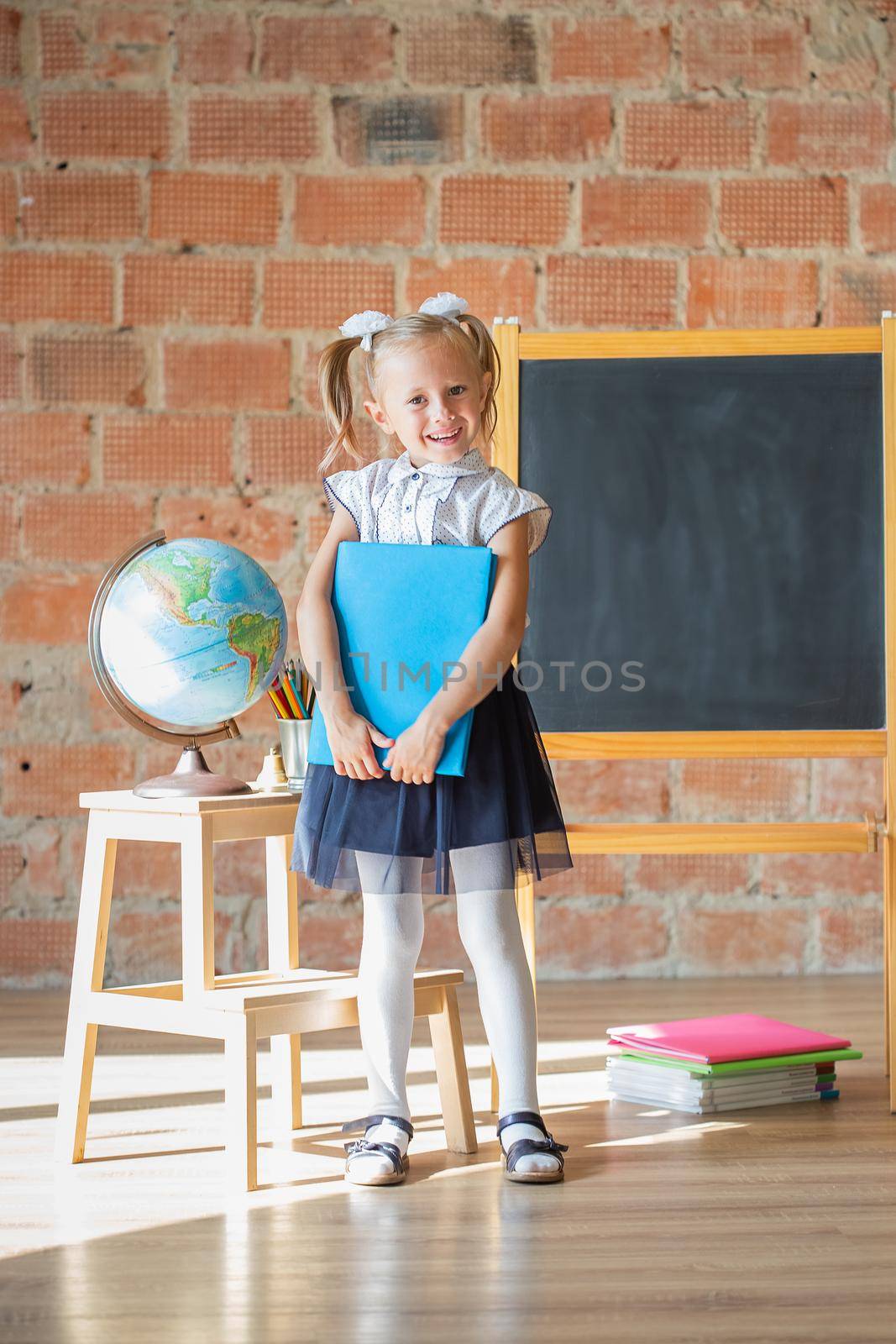 Adorable schoolgirl smiling in front of blackboard with book in her hands by galinasharapova