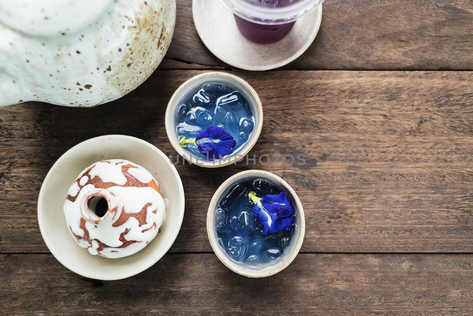 Clay pot of  iced butterfly pea tea on wooden table