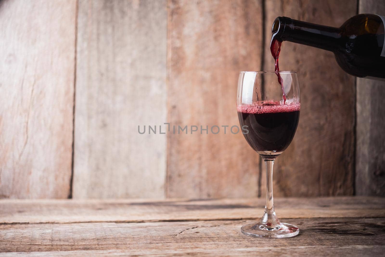 pouring wine into glass on wood background by Wmpix