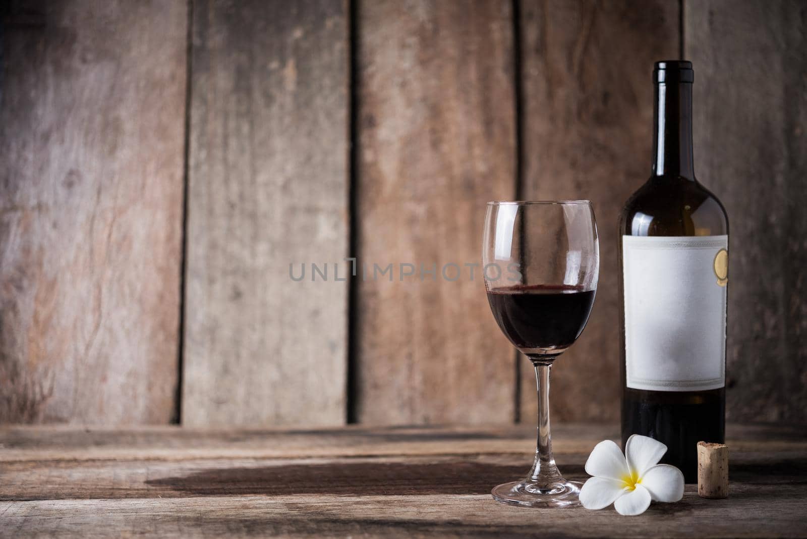 Wine bottle, glass and white flower on wood background