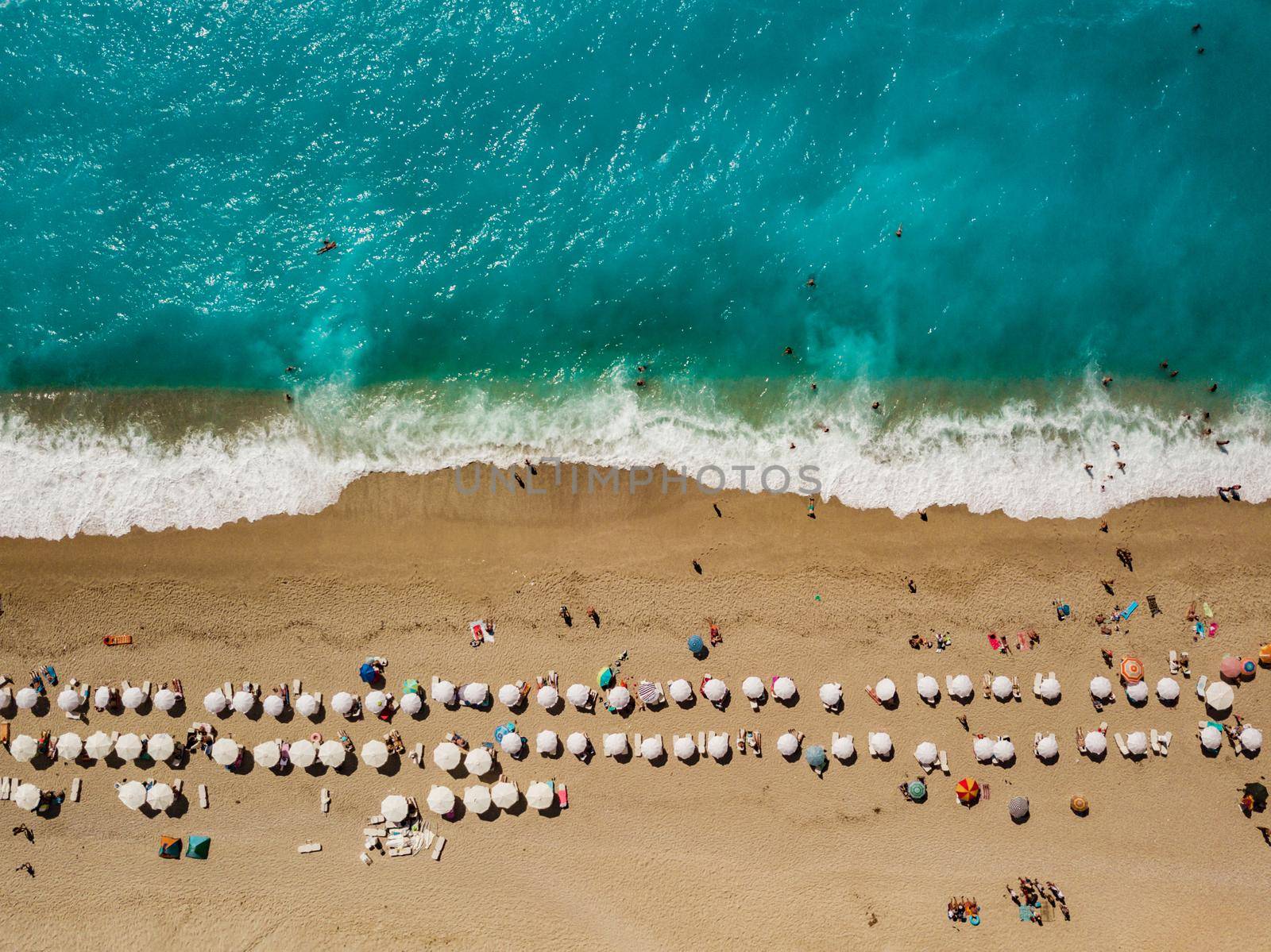 Aerial view of the amazing  idyllic  beach with white umbrellas, sunbed and people who sunbathing and swiming.