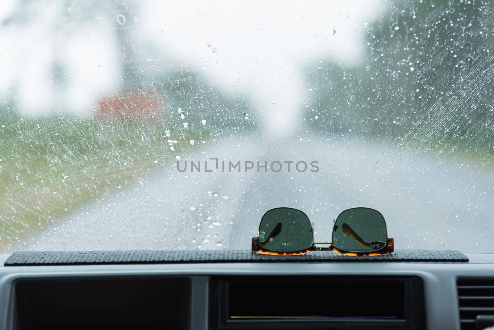 Sunglasses on console car with background is the sea in front of car in the rainy day