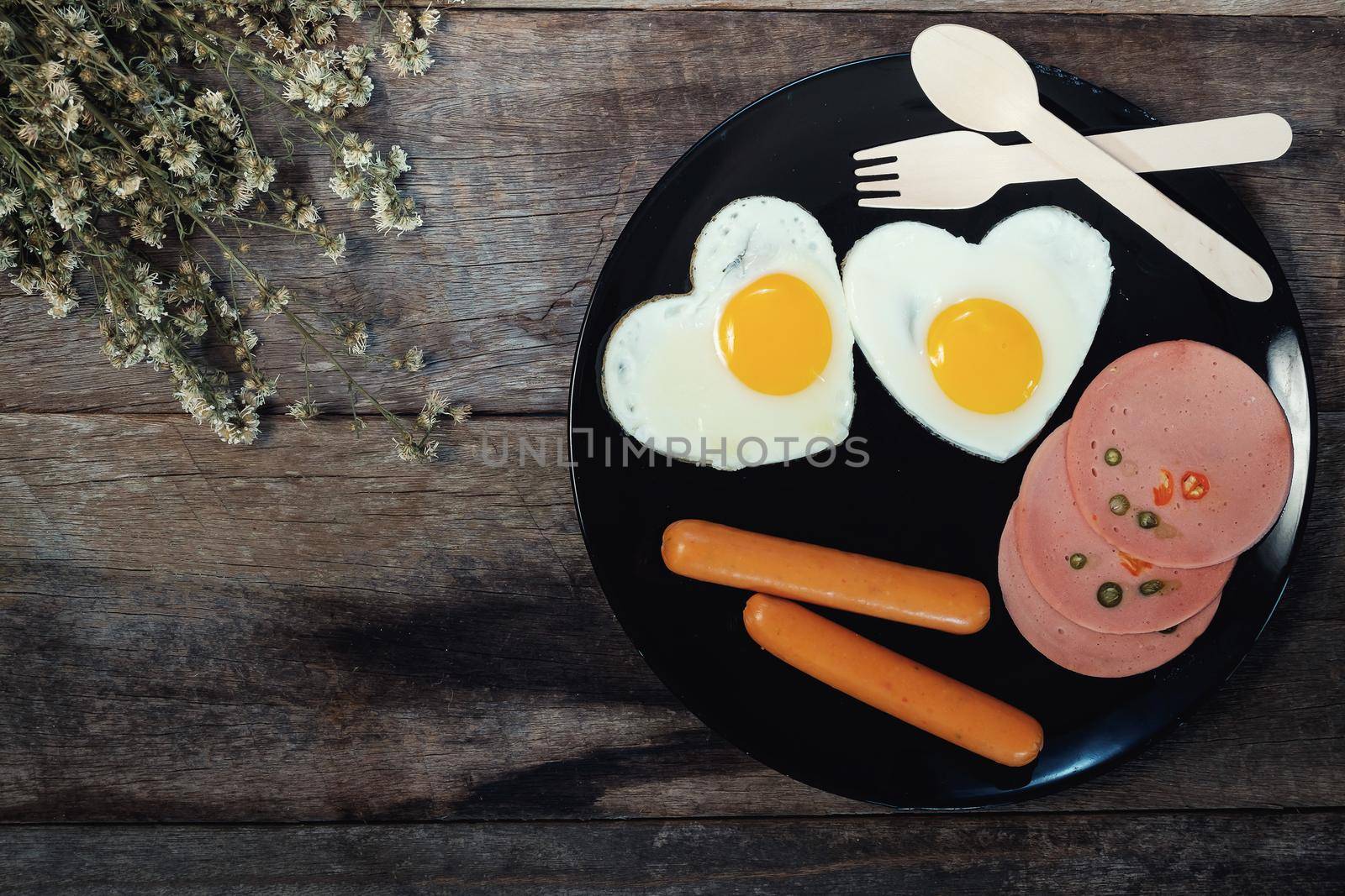 Fried egg on heart-shaped with ham and sausage on wood table