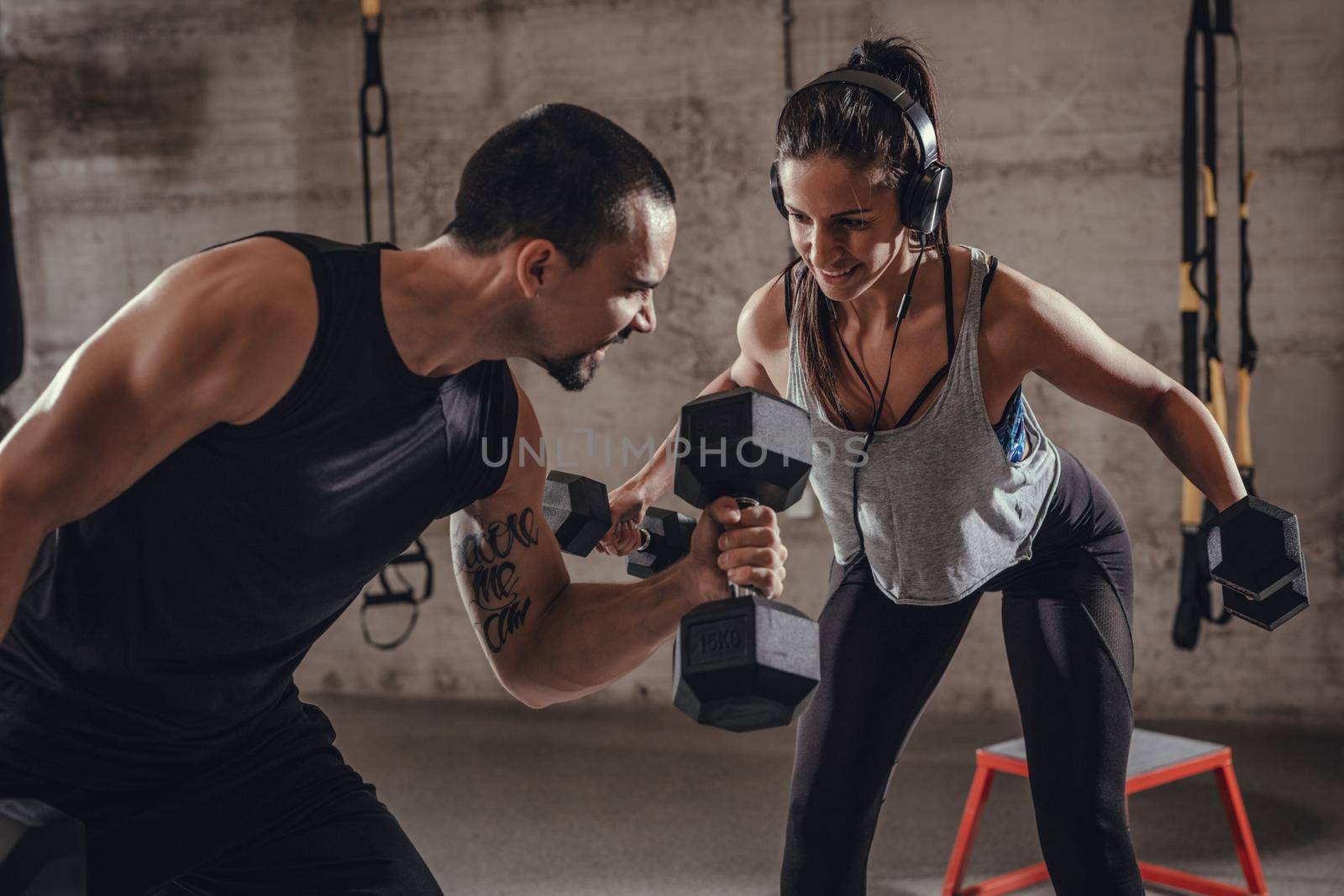 Young muscular couple doing hard exercise with dumbbells for shoulders on cross fit training at the gym.