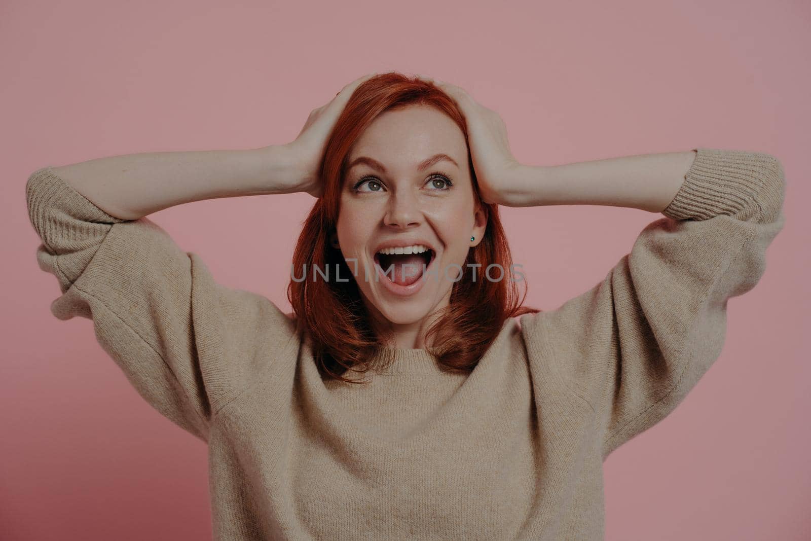 Surprised shocked european female holding head in hands and looking upside with excited expression and opened mouth, hearing about big sale prices, standing in studio isolated over pink background