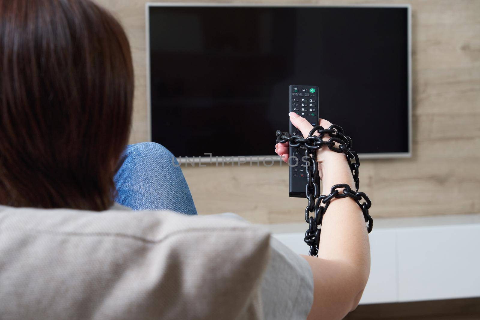 TV addiction and dependency concept. Female hand tied to the remote with the chain
