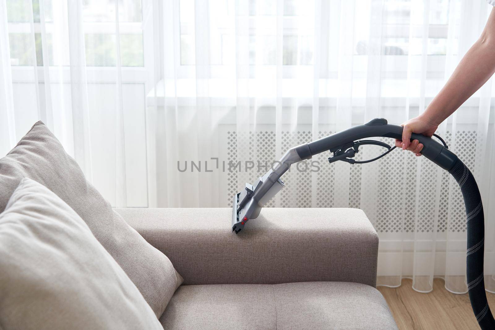 Young housewife Cleaning the Sofa with Vacuum Cleaner in living room