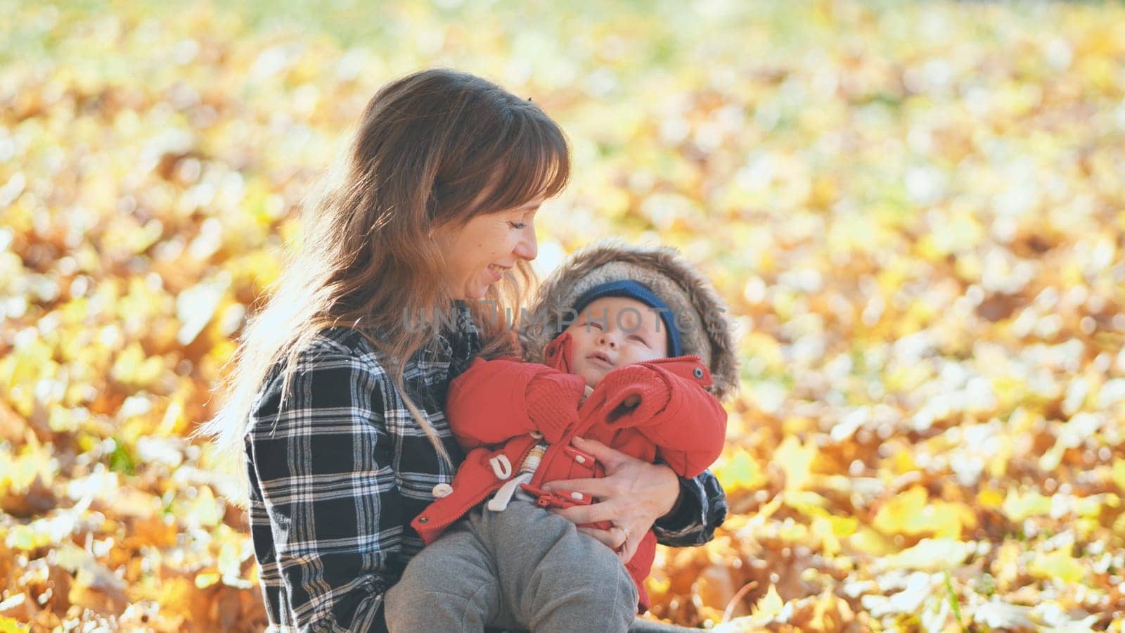 A mother and child in the park in the fall sitting on fallen leaves