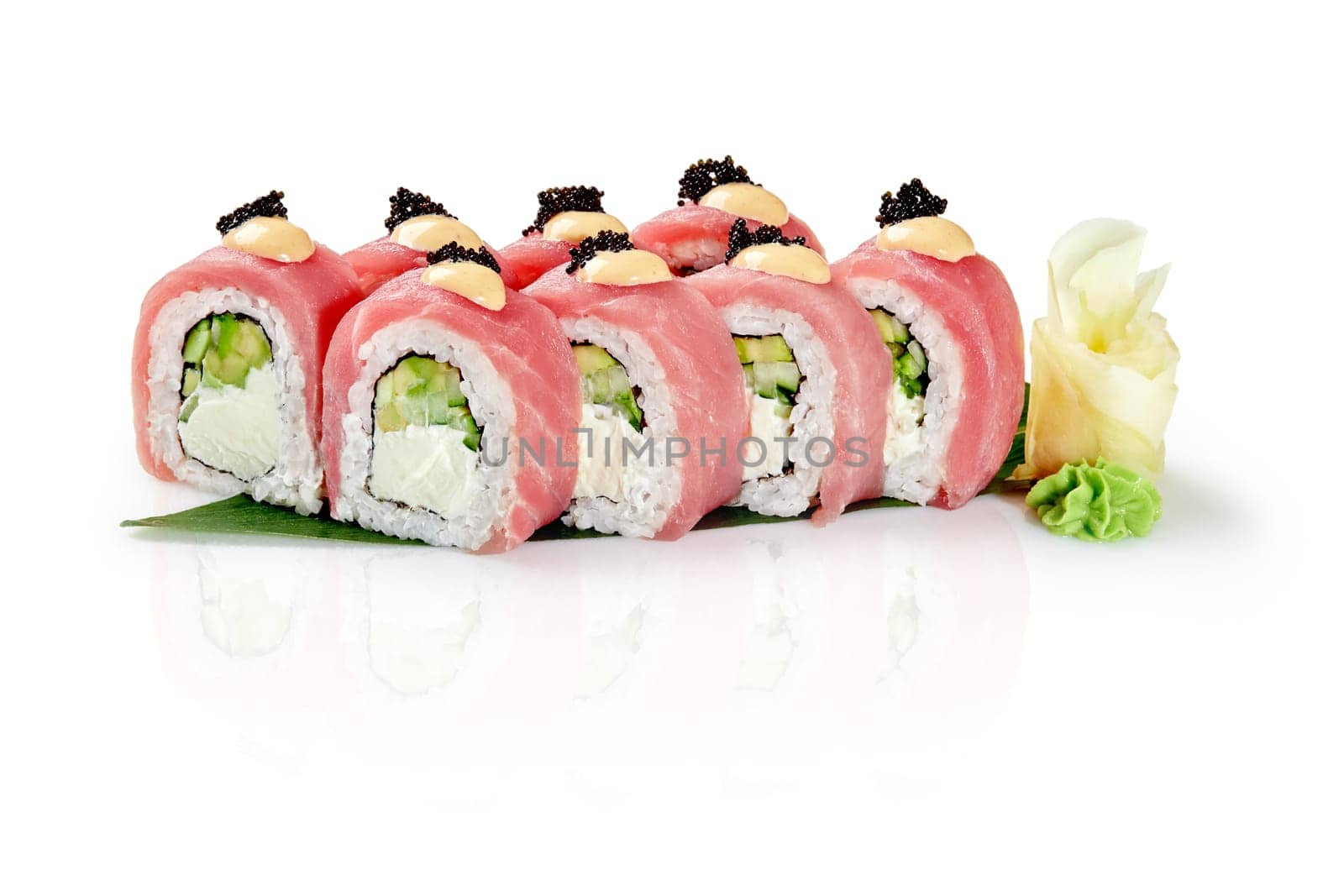 Appetizing Philadelphia sushi rolls filled with cream cheese and cucumbers topped with fresh tuna fillet, spicy sauce and black tobiko served with wasabi and pickled ginger on bamboo leaf