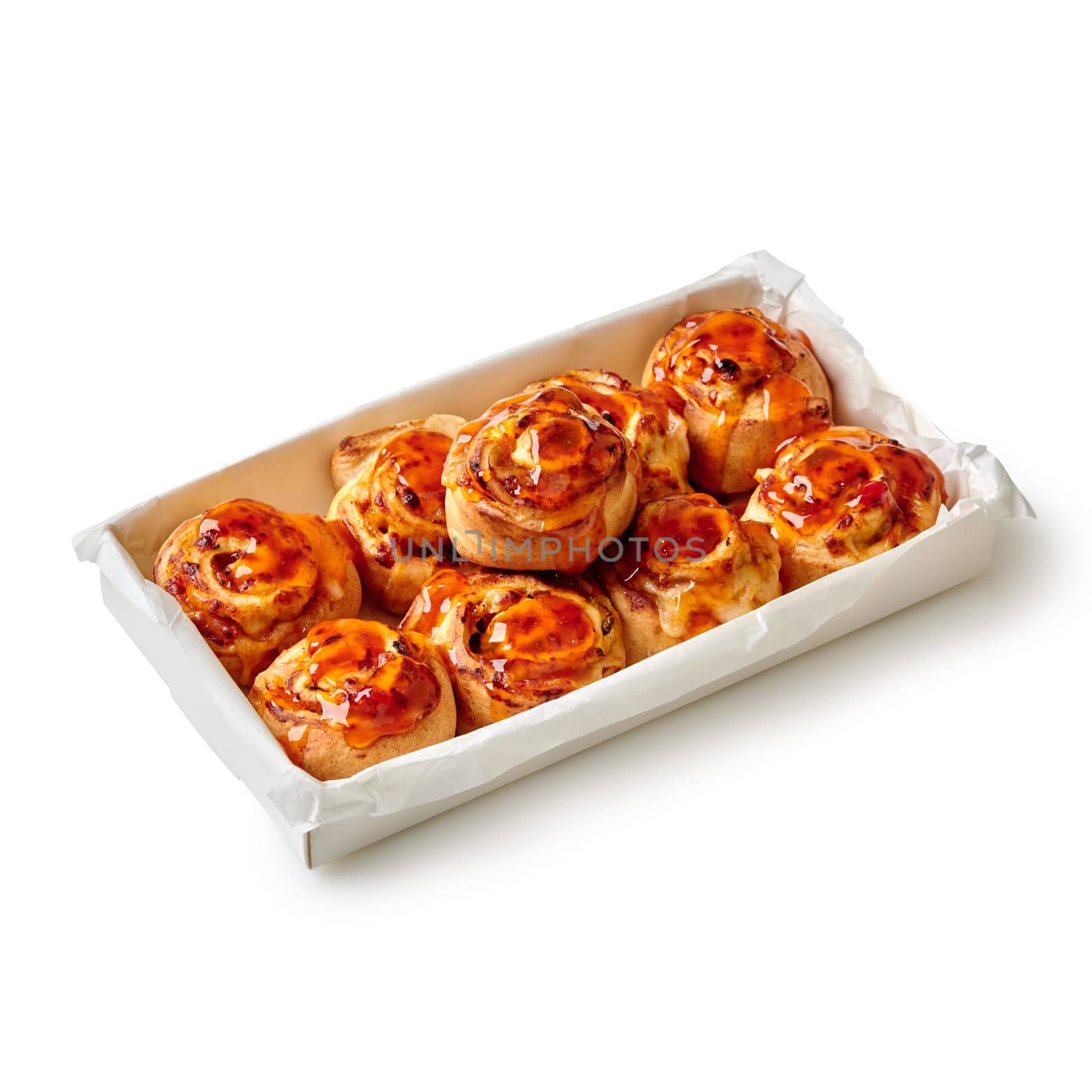 Appetizing fluffy freshly baked rolled buns with custard topped with flavorful honey packed in paper box isolated on white background. Popular sweet pastries