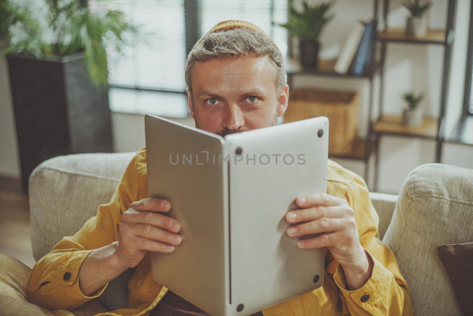 Humorous stock photo concept of bad student who engaged in unproductive studying habits. Guy holding laptop if it were book, highlighting lack of focus and attention to task at hand. High quality photo