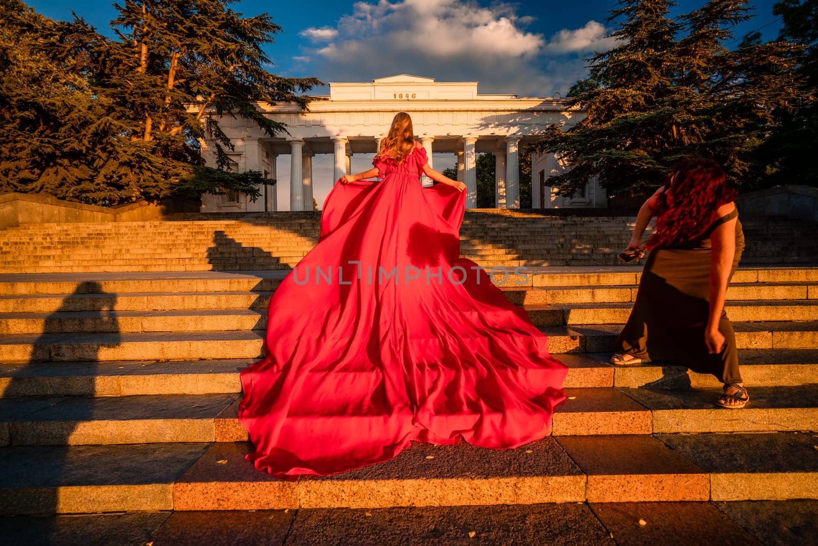 Sunrise red dress. A woman in a long red dress against the backdrop of sunrise, bright golden light of the sun's rays. The concept of femininity, harmony. by Matiunina