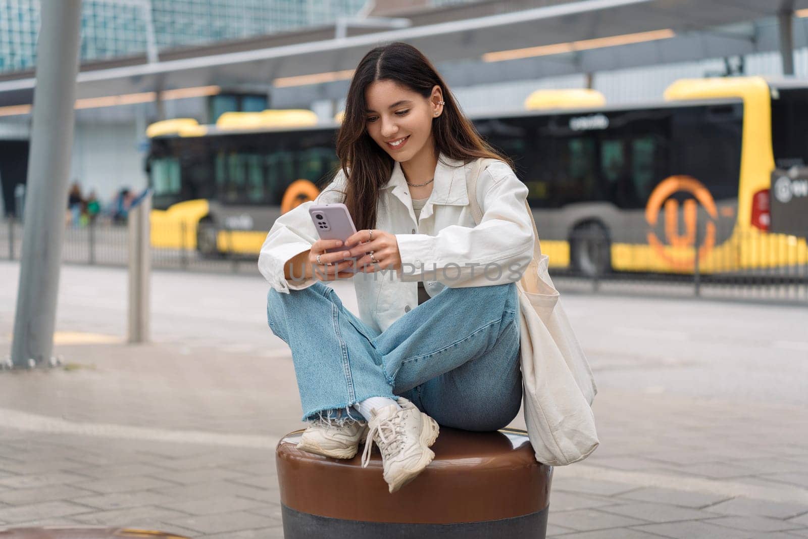 Checking public transport timetable. Multi-ethnic attractive woman with beautiful smile at bus station looking at the phone.