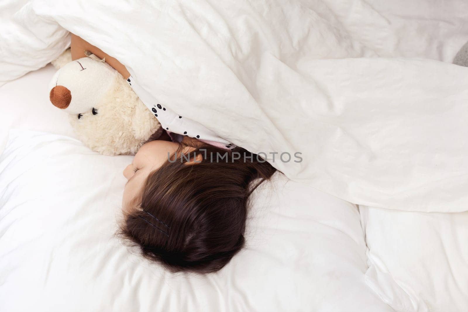 Cute little child girl sleeping with teddy bearin her bed. top view