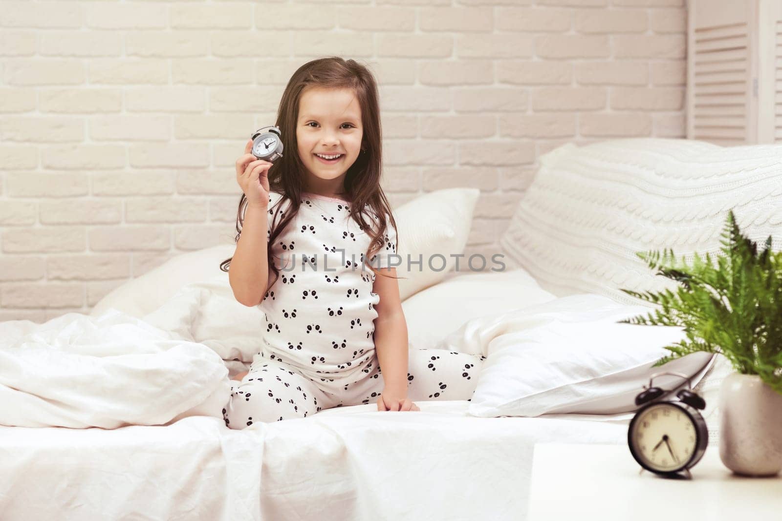 cute happy little child girl in pyjamas with clock in bed. good morning