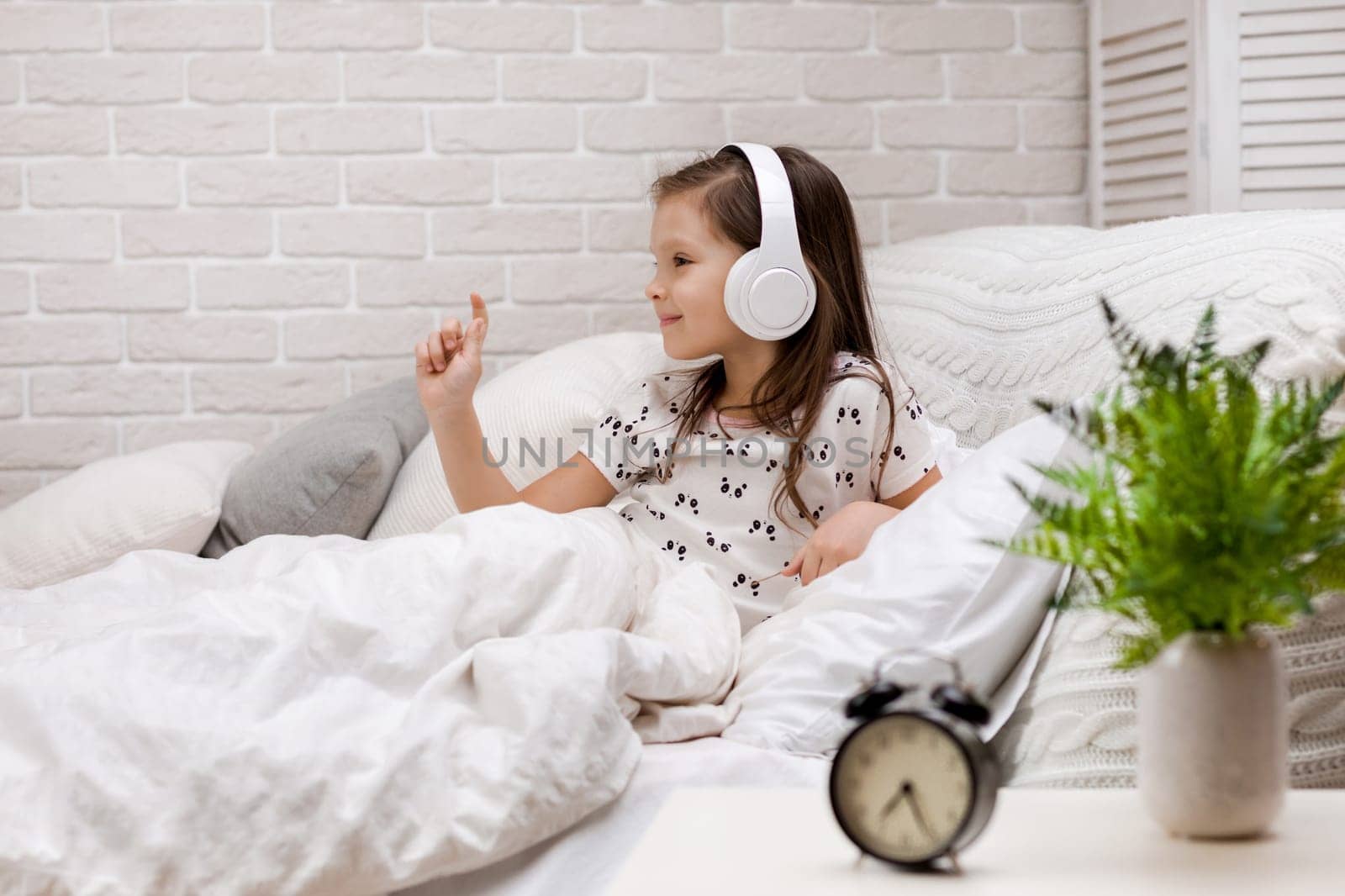 little child girl listening to the music with the headphones and dancing on bed. happy morning