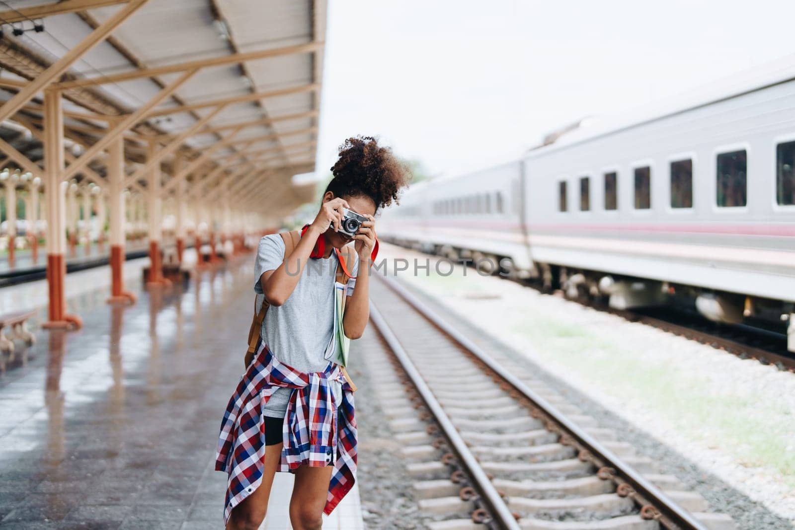 Asian teenage girl african american traveling using a camera take a photo to capture memories while waiting for a train at the station. by Manastrong