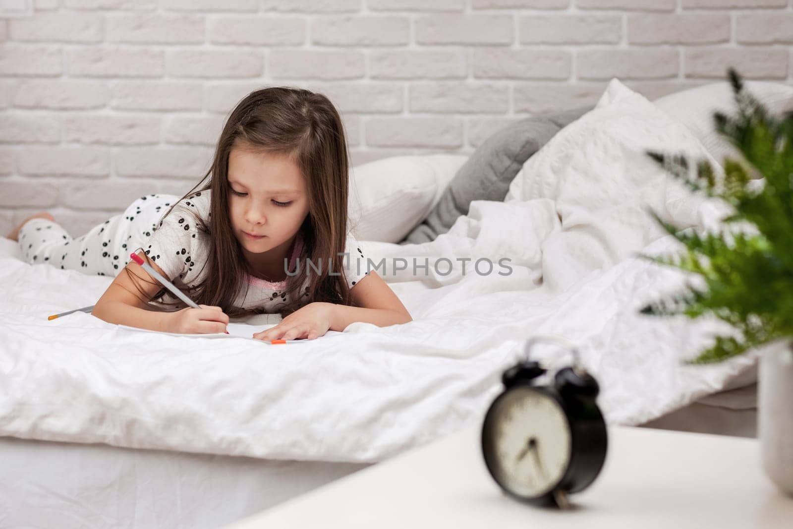 cute little girl drawing pictures while lying on bed. Kid painting at home