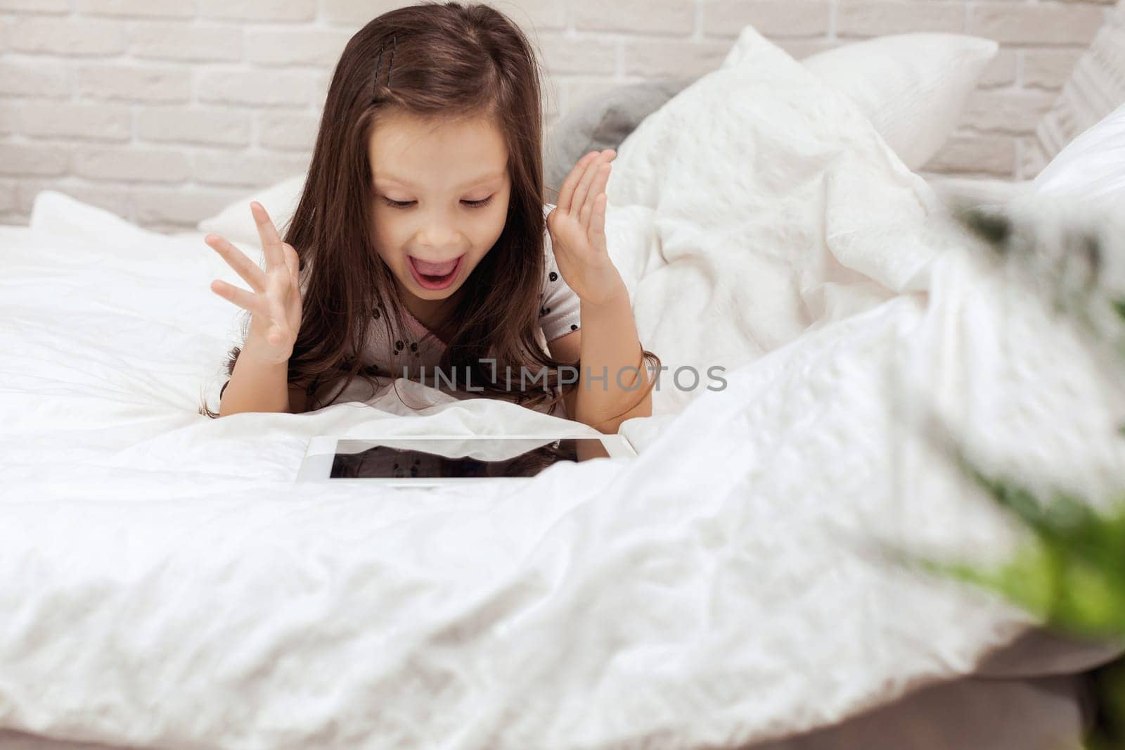 cute little child girl lies in bed uses digital tablet. child playing on tablet pc.