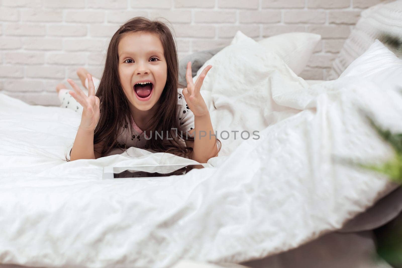 cute little child girl lies in bed uses digital tablet. child playing on tablet pc.