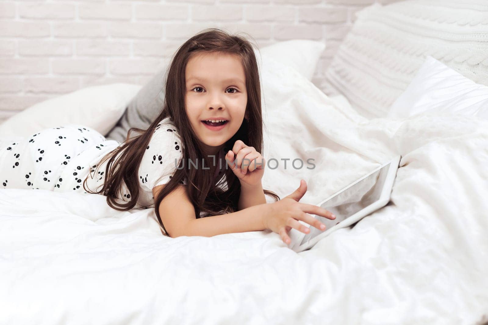 cute little child girl lies in bed uses digital tablet. child playing on tablet pc.