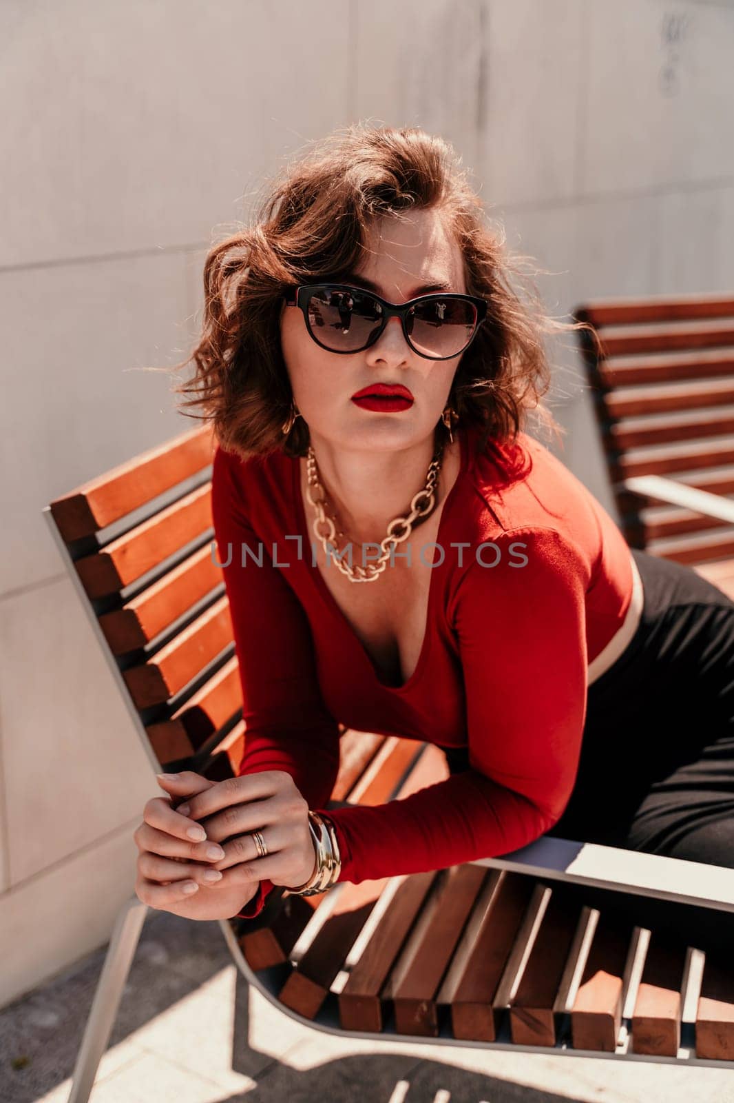 Portrait of a woman on the street. An attractive woman in glasses, a red blouse and a black skirt is sitting on a bench outside. by Matiunina
