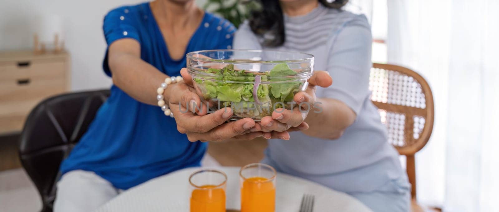 Two old women eat salad healthy food at living room.