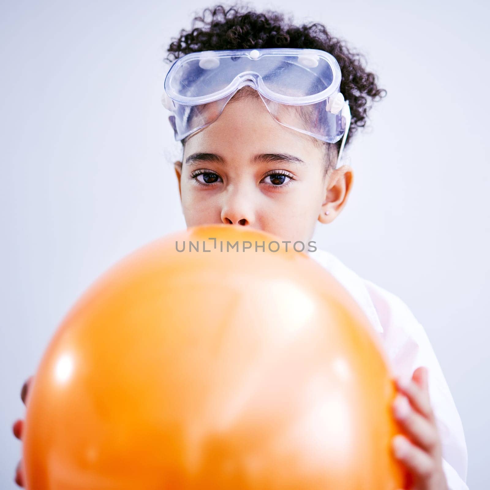 Portrait, science and a kid blowing a balloon in studio on a gray background for a childhood experiment. Children, education and laboratory with a female child wearing goggles while learning by YuriArcurs