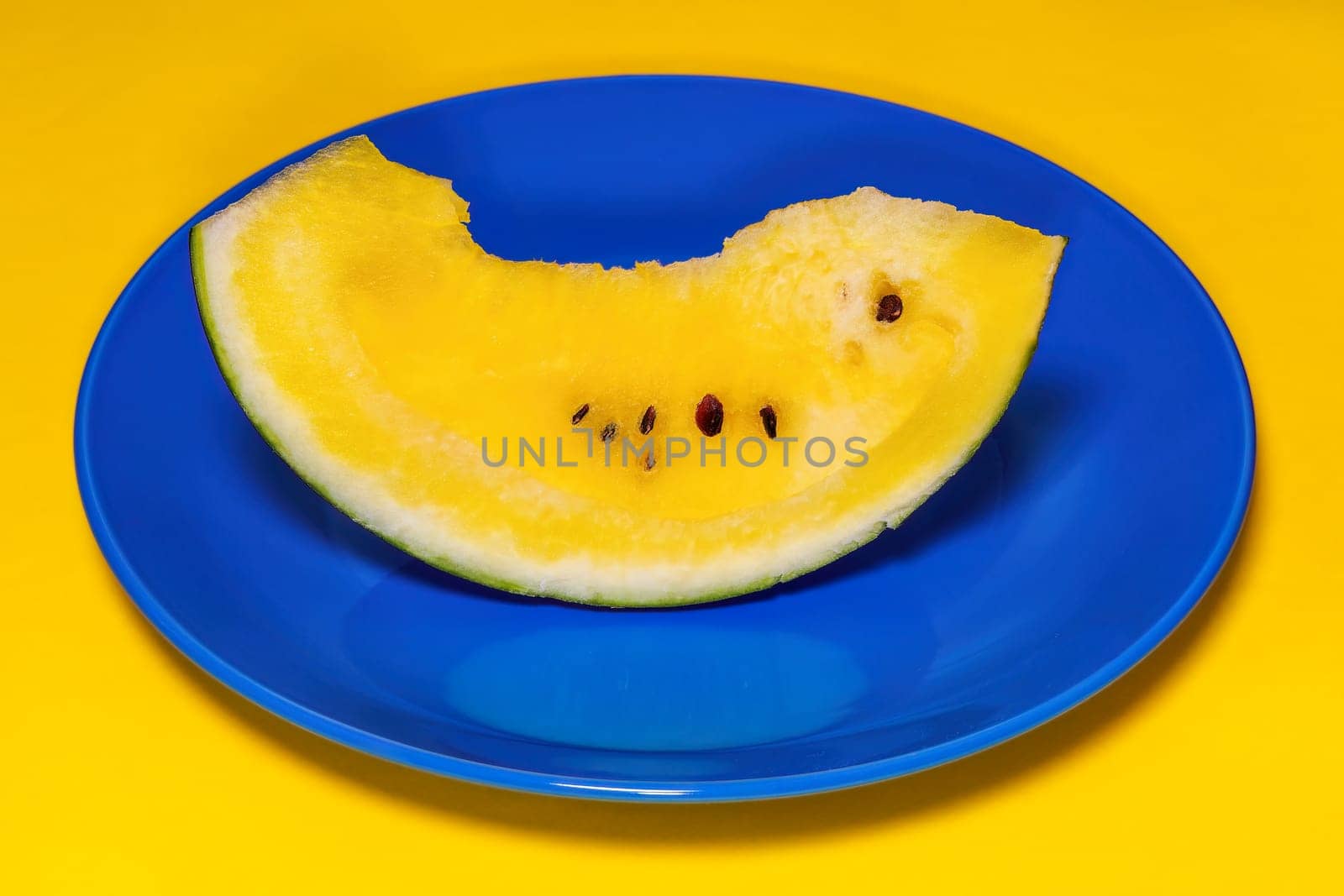 A slice of sweet fresh yellow watermelon served on a blue dish, against colorful background.