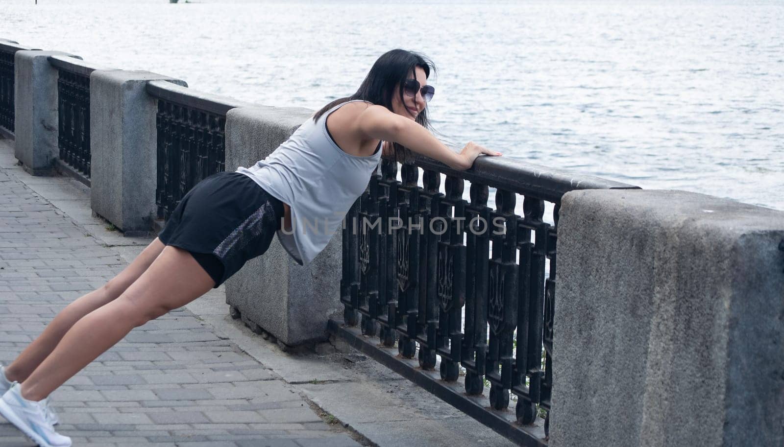 The girl is slim, tall and athletic in short shorts, doing push-ups on the street in the summer near the river. Sports concept. by ketlit