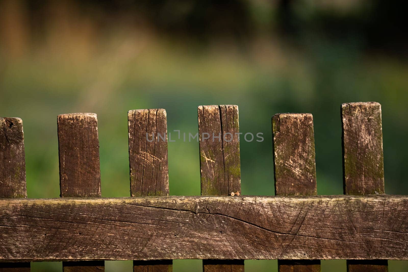 Close frame of wooden old fence built of rails. The background is heavily blurred in shades of green and brown.