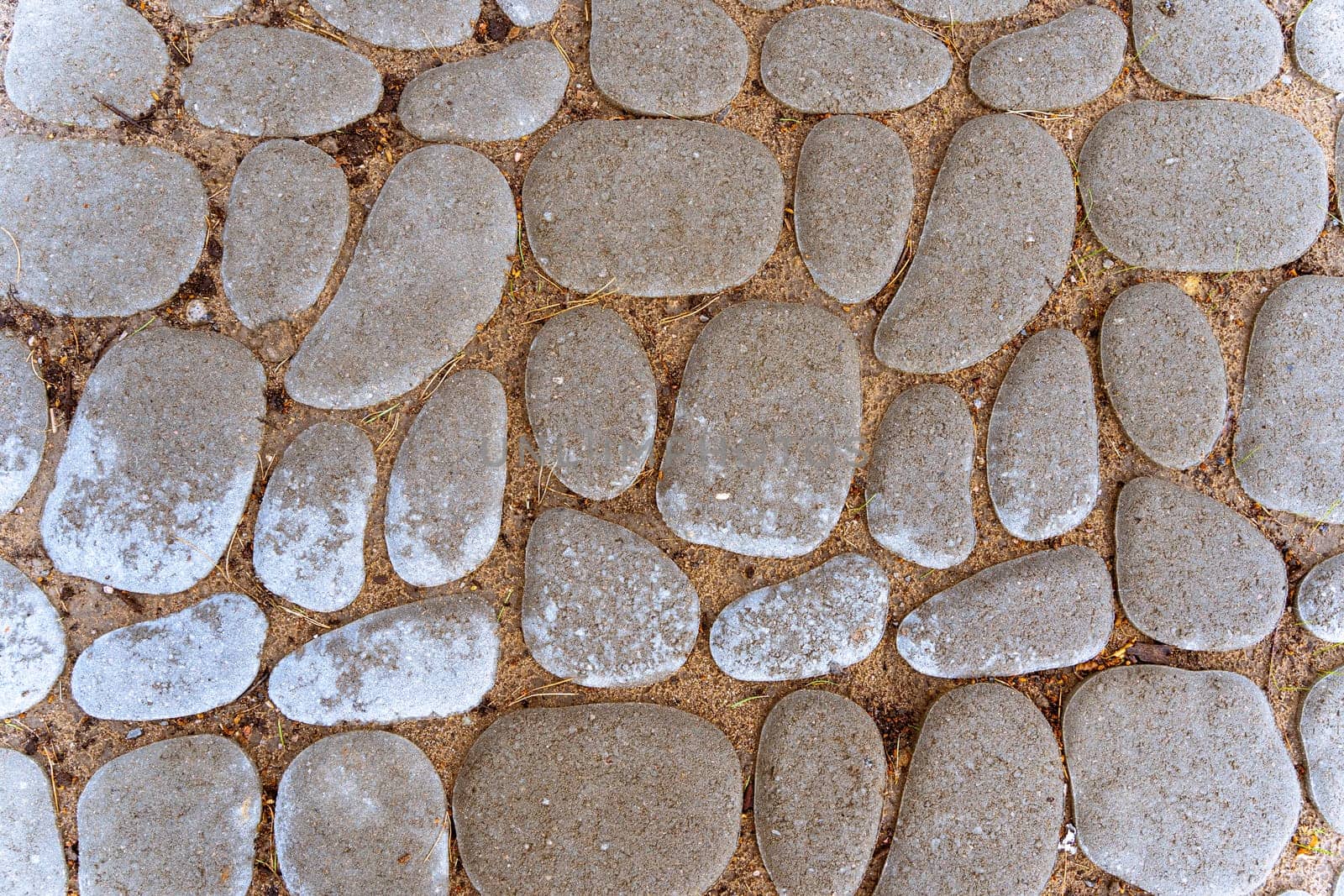 A stone path in a park or city garden. Background of cobblestone pavement. The texture of the stone pavement. A stone-paved road. cobblestone pavement close-up. Sidewalk design. overhead view