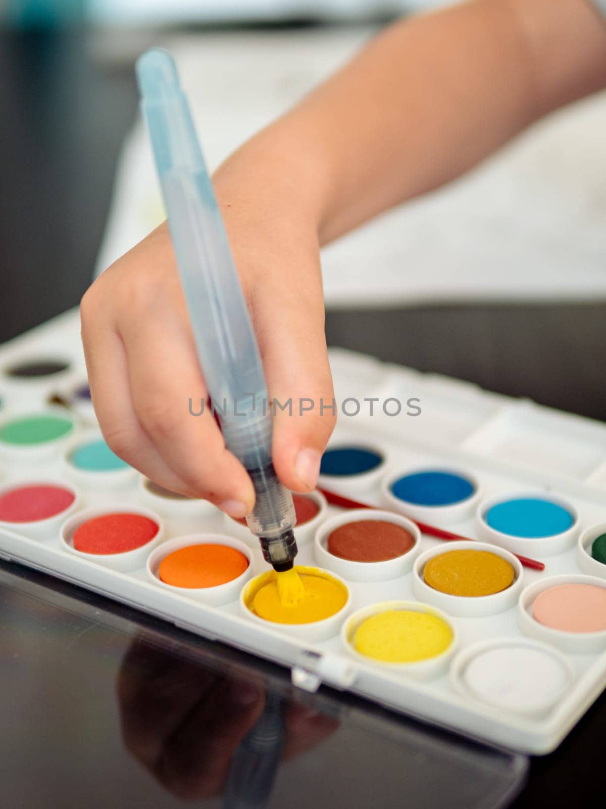 The boy paints with watercolors. Child picking up paint on brush, use brush with integrated water container or water brush. Close up, focus on waterbrush