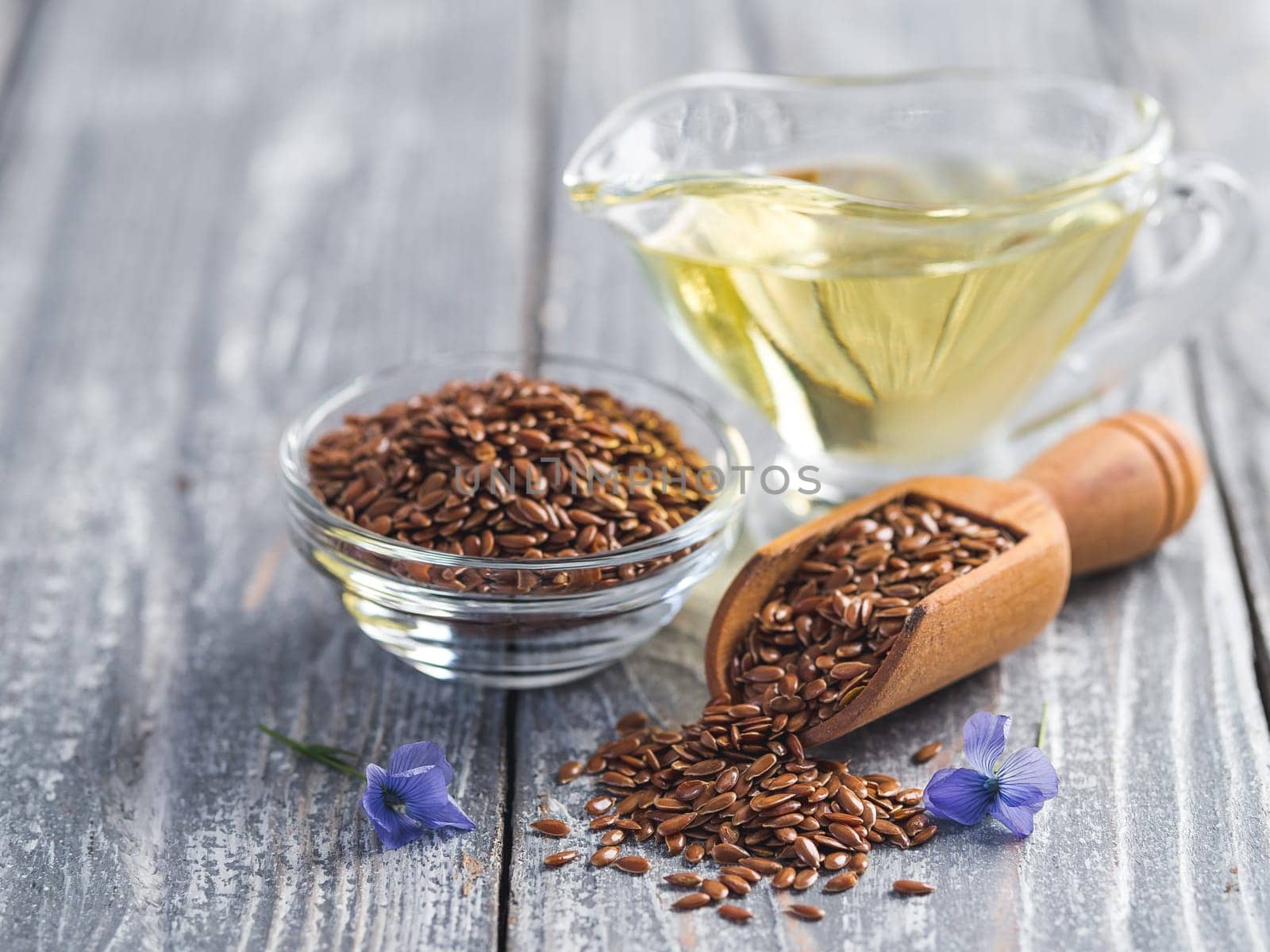 Flax seeds and flax oil. Brown linen seeds, flaxseed oil and blue flax flowers on old gray wooden background. Copy space