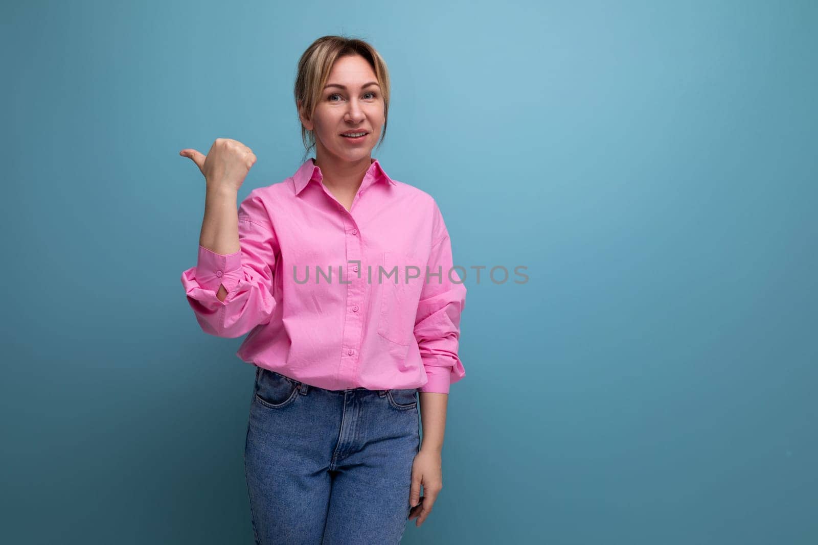 stylish young blond businesswoman in a pink shirt and jeans gesticulates inspiredly and talks about the idea of a business on a studio background with copy space.