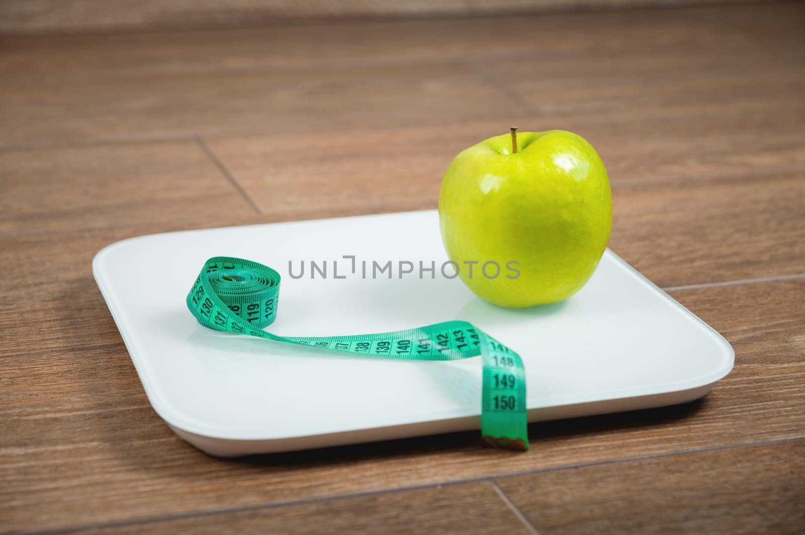 Scale with measuring tape on white scales. Weight loss concept. Fresh apple and measuring tape on scales standing on the floor, close-up.