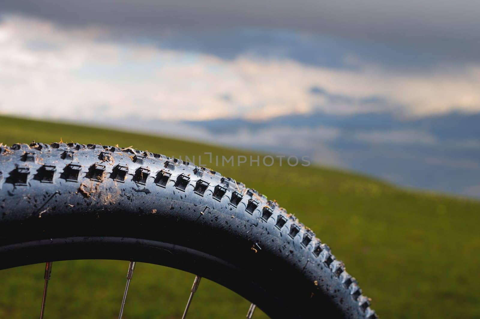 mountain bike tire with spikes close-up, with blurred background of green mountain fields and cloudy sky. place for text.