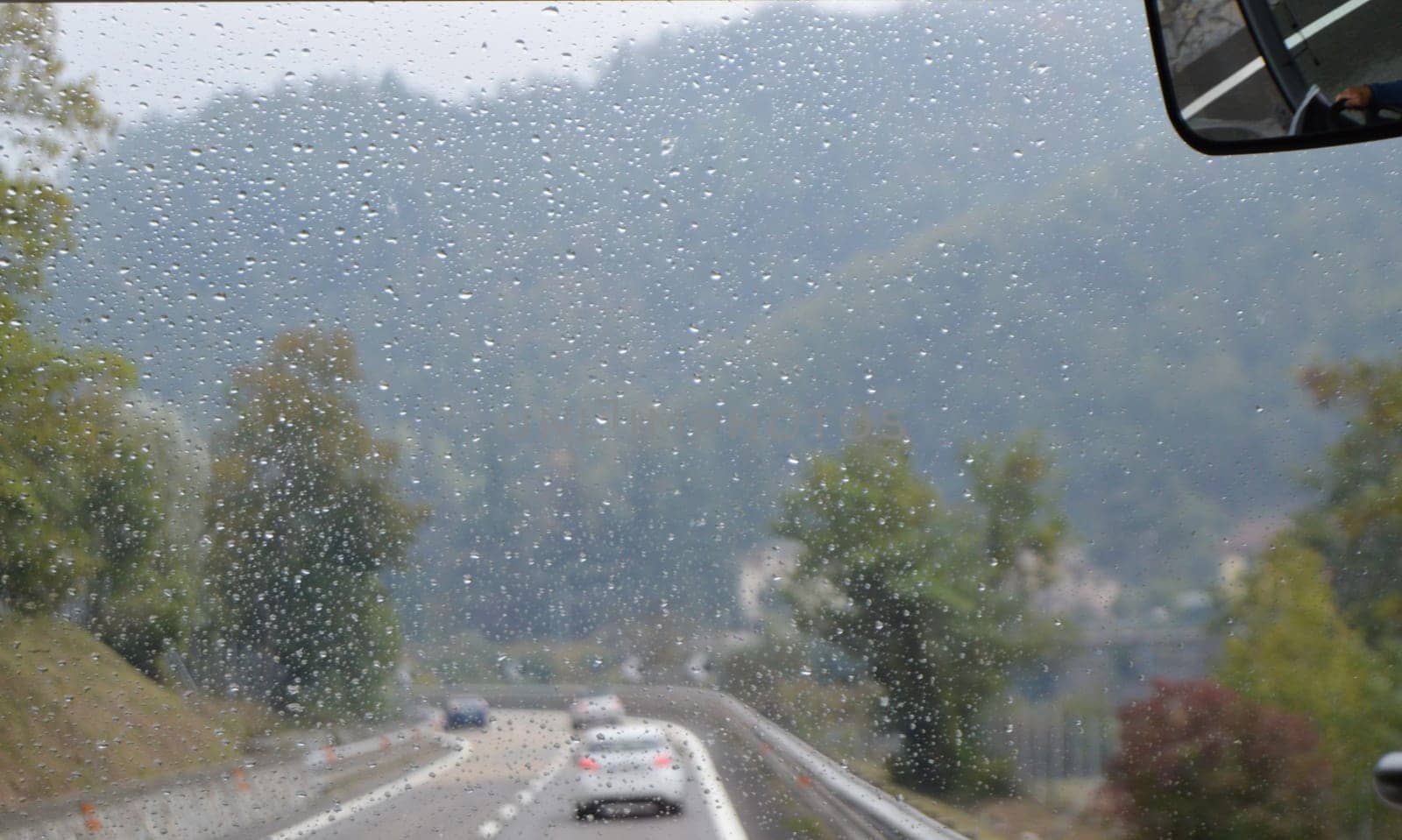 View from the windshield of a car in the rain. Mountain landscape and highway in bad weather.