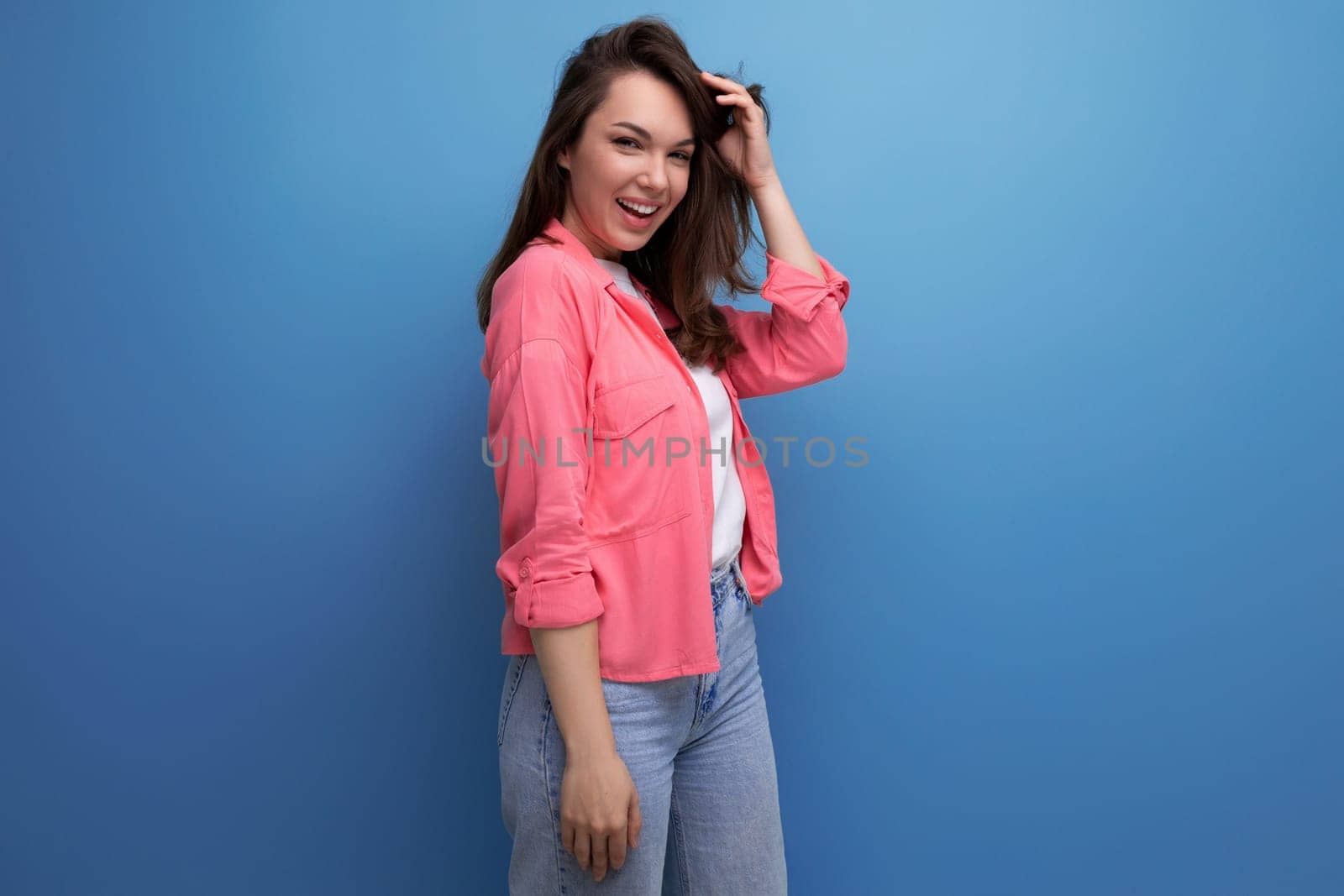 portrait of a brunette woman in a shirt and jeans posing with a smile on a studio background.