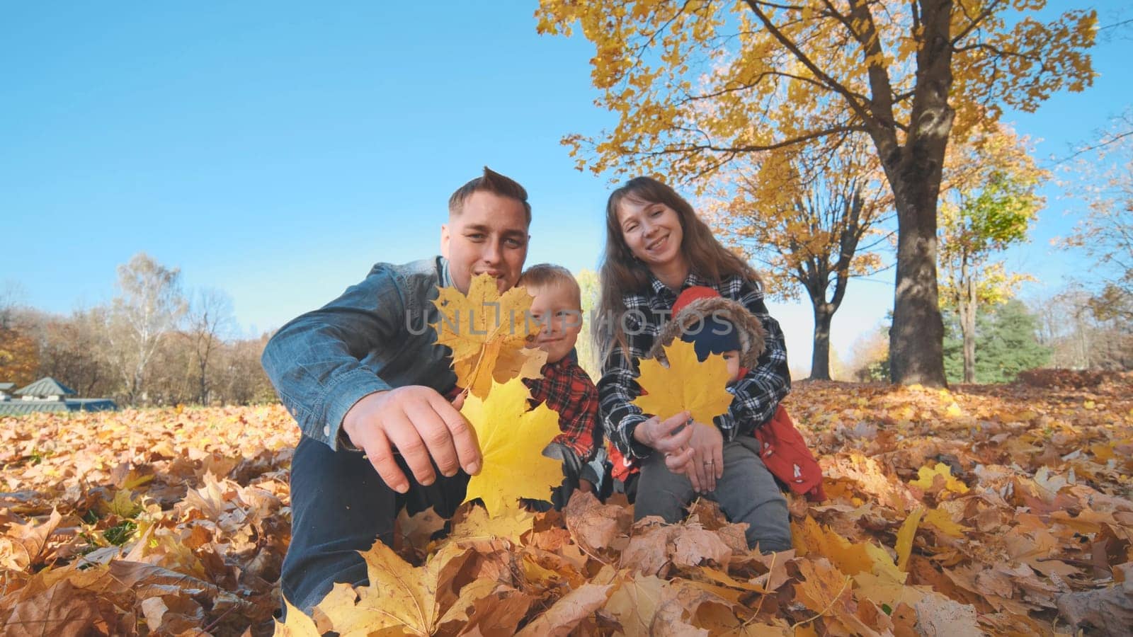 A happy family covers the camera lens with a stiff autumn leaf