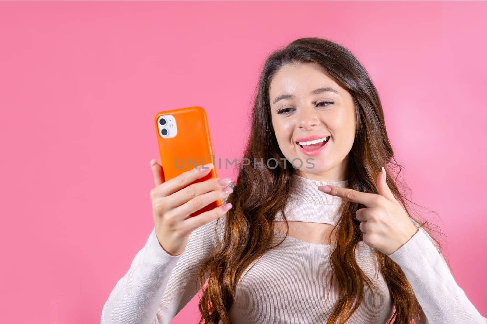 Portrait of woman shows by finger on mobile phone excited about the new app on the pink background