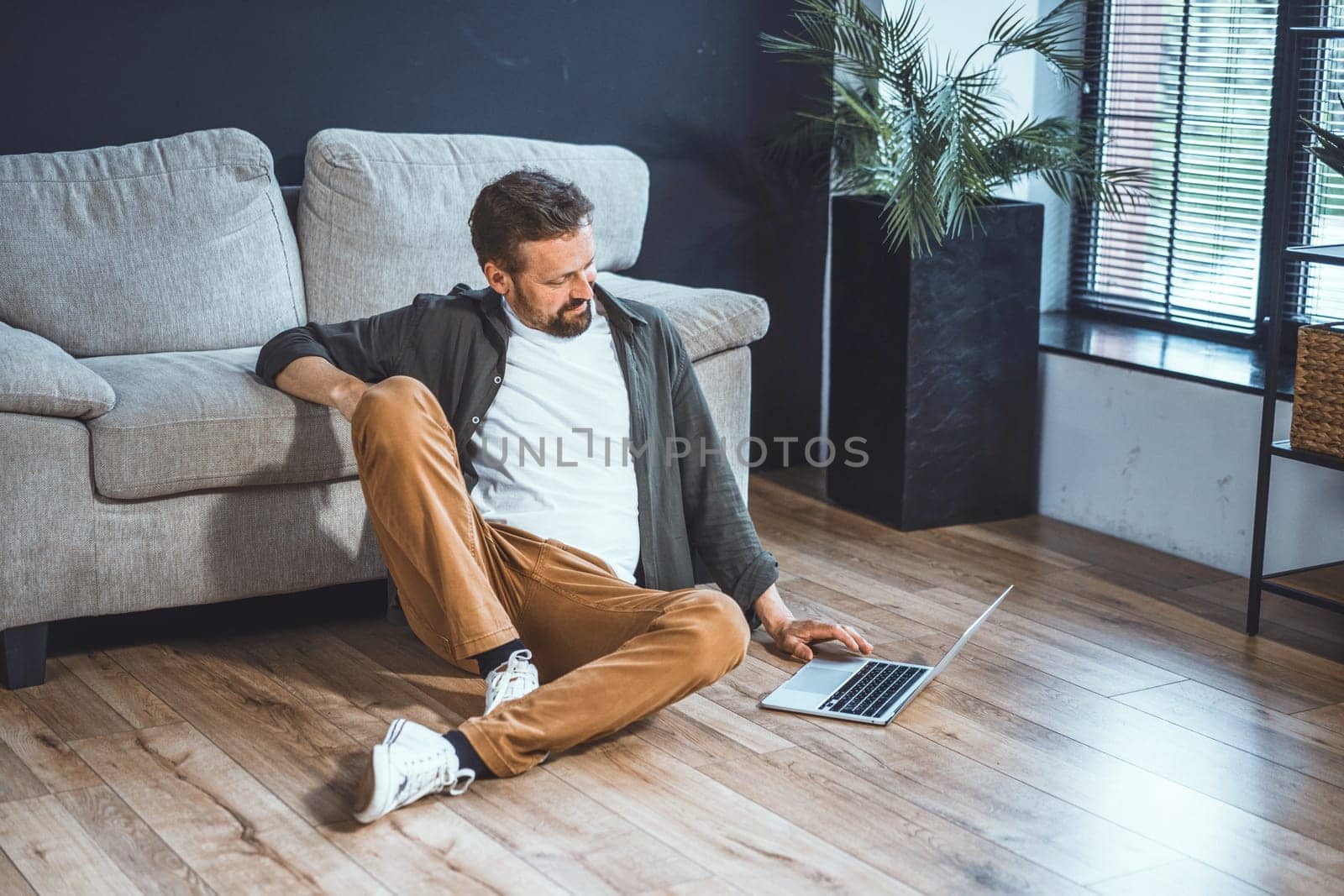 Lazy and handsome man spending time home. Man sitting comfortably, browsing internet on laptop. With relaxed posture and casual vibe, he online search, possibly looking for information. High quality photo