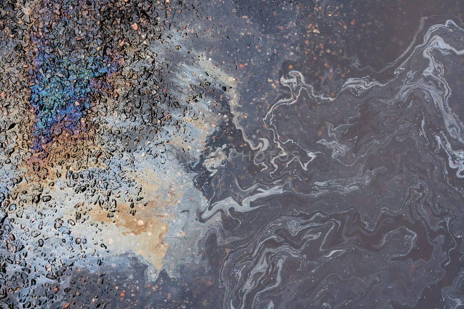 Oil stains from leaks in the car engine. Oil after rain makes spots with rainbow reflections refractive sun spectrum. Beautiful color mosaic, abstraction, ecology